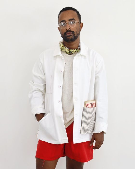 A model wearing the white jacket featuring a striped pocket holding a book, along with additional smaller pockets