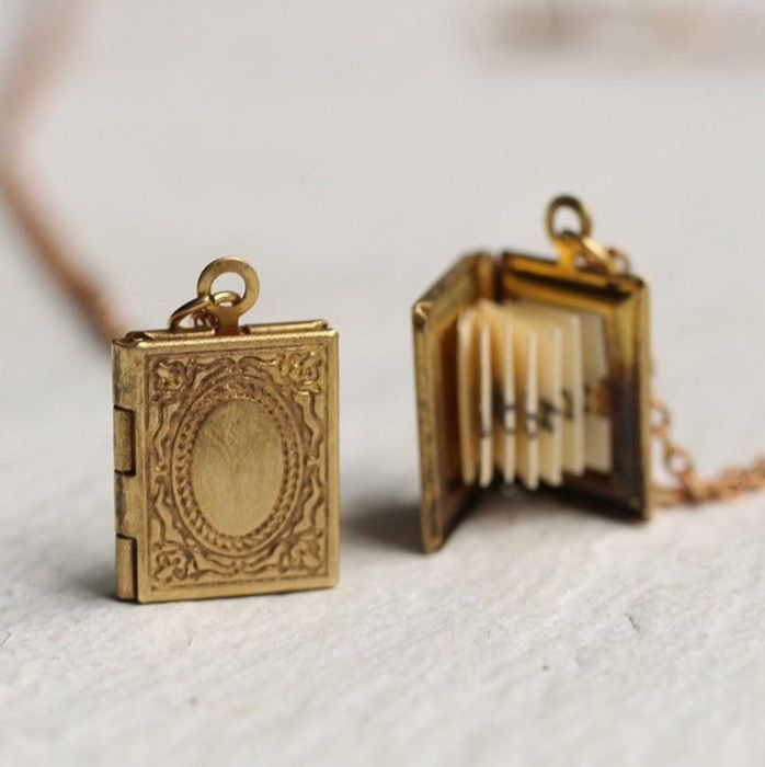 The gold-toned locket designed to resemble an antique book, shown open to display the intricately pleated paper message inside.