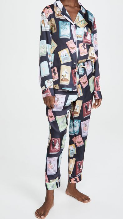 A model wearing the pajamas featuring a black background with pastel-colored book designs, including titles like Dracula, The Great Gatsby, Moby Dick, Black Beauty, and others