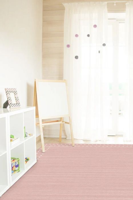 A pink Ruggable rug with a white polka dot border in a playroom