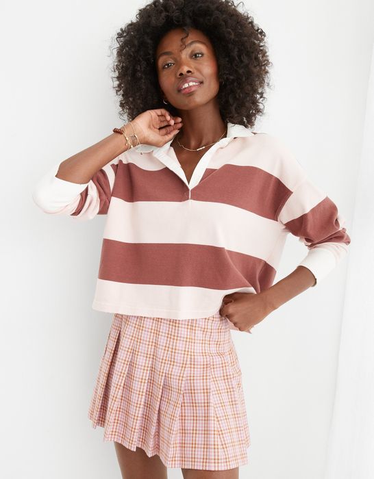 The model is wearing a slightly cropped, faded pink and red long-sleeve polo shirt.