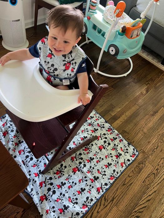 A baby in a highchair with a Mickey Mouse mat underneath