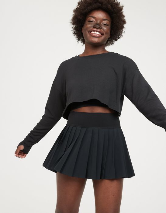 The model is wearing a short black pleated tennis skirt.