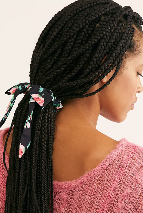 a model styling her braids into a ponytail using the floral print scrunchie