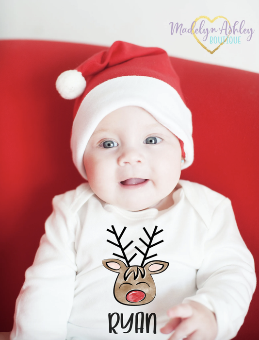 A baby wearing a white long-sleeve bodysuit featuring a reindeer design and the name 