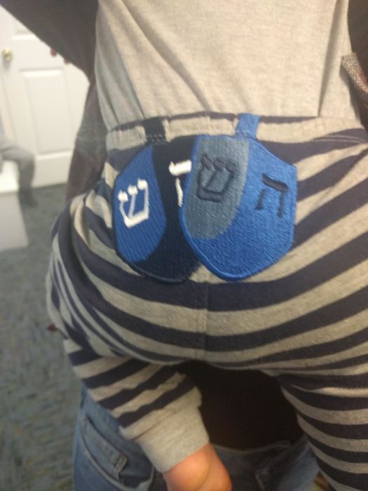 A reviewer's baby dressed in the outfit with dreidels on the backside.