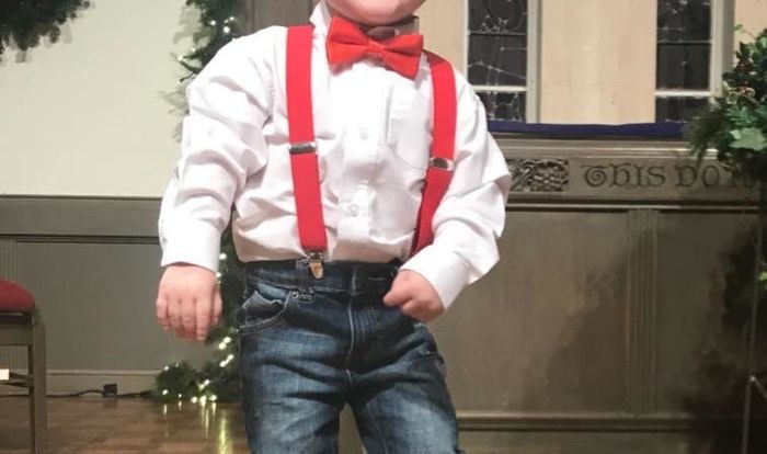 A child wearing a red bow tie paired with suspenders, a dress shirt, and jeans.