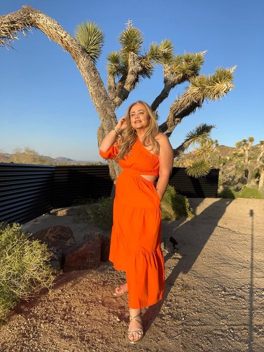A reviewer wearing the orange one-shoulder maxi dress with a ruffle design, highlighting its vibrant color, unique style, and suitability for summer events.