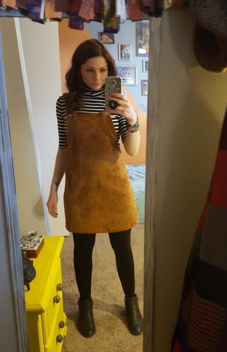 reviewer wearing the pinafore layered over a striped turtleneck and black tights