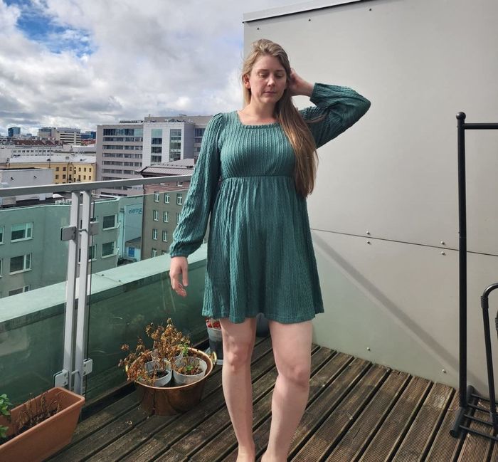 A reviewer is photographed outdoors, elegantly wearing the teal dress.