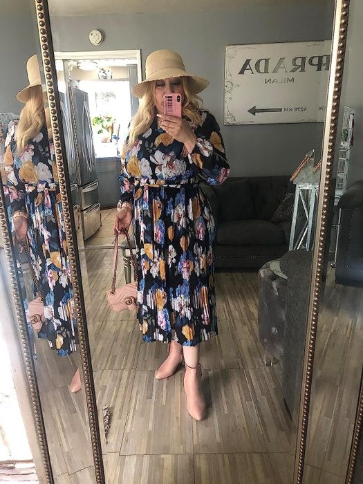 A reviewer wearing a black colorful floral-print long-sleeve midi dress paired with pink boots, sharing their thoughts on the outfit.