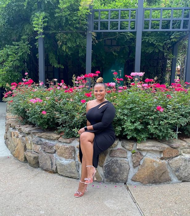 A reviewer wearing a black one-shoulder ruched midi dress, sharing their experience with its fit and style.