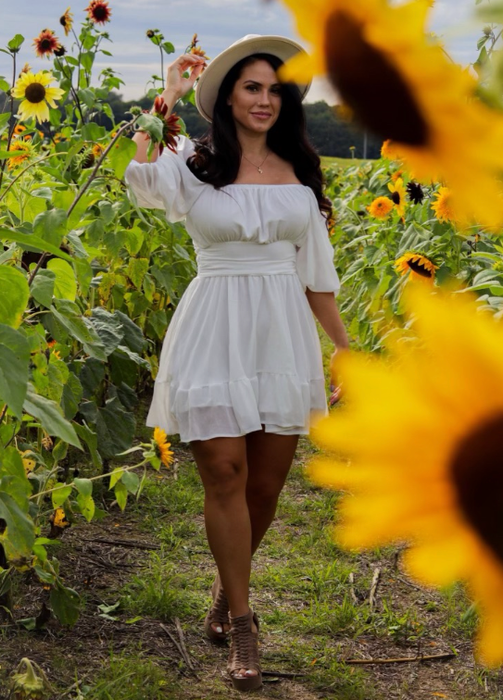 A reviewer wearing a white dress in a sunflower field