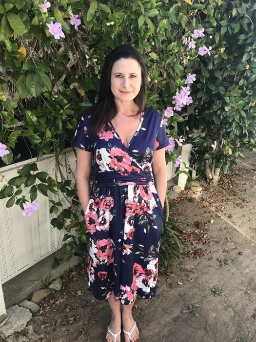 The reviewer is standing gracefully in a blue dress adorned with floral patterns.