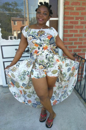 A reviewer wearing the white dress featuring orange and green floral patterns, lifting the sides to show the shorts underneath