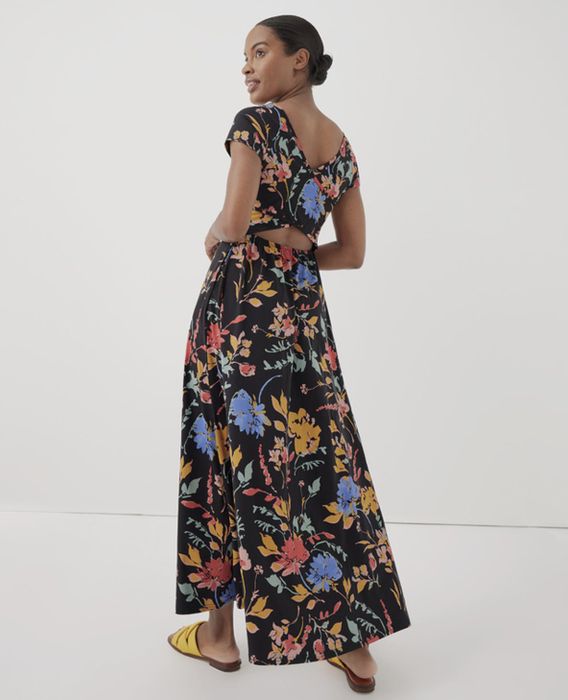 A woman in a floral dress featuring a back cut-out detail, posing for a shopping feature