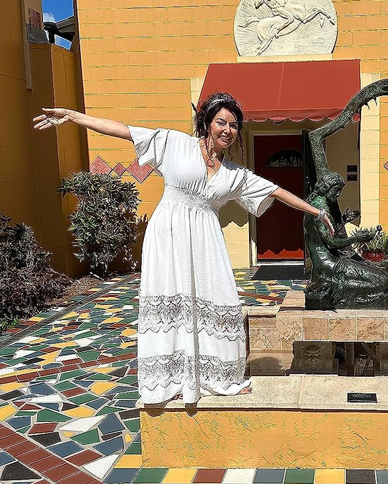 The reviewer is wearing a chic white dress outdoors.