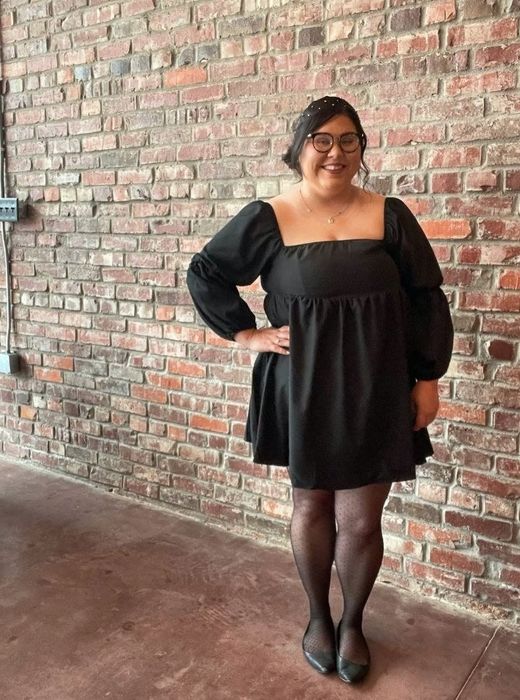 A reviewer wearing a black mini dress with a square neck and puff sleeves