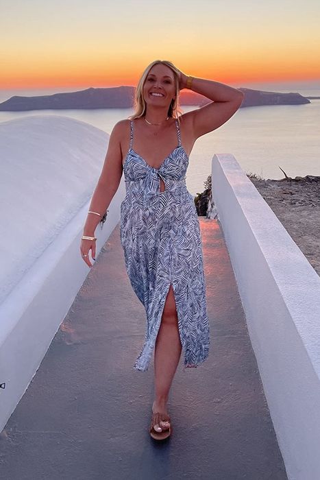 A reviewer wearing a sleeveless tie-front satin dress featuring a black and white leaf print.