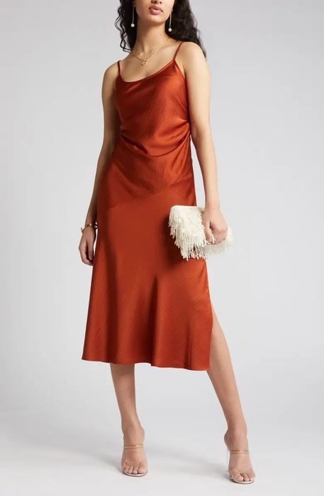 A model in an orange dress, accessorized with a white bag and clear sandals.