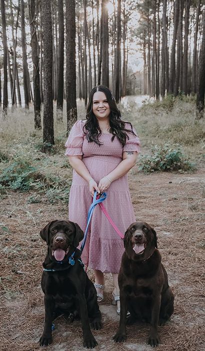 A reviewer wearing a pink dress, accompanied by two adorable chocolate labs.