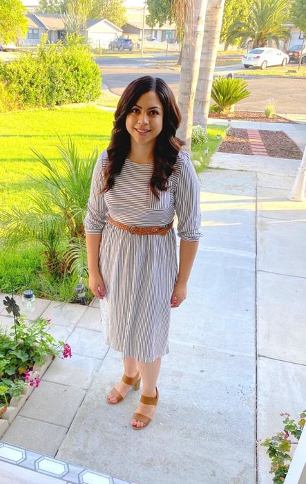 A reviewer rocking a black and white striped dress, paired with brown shoes and a matching belt.