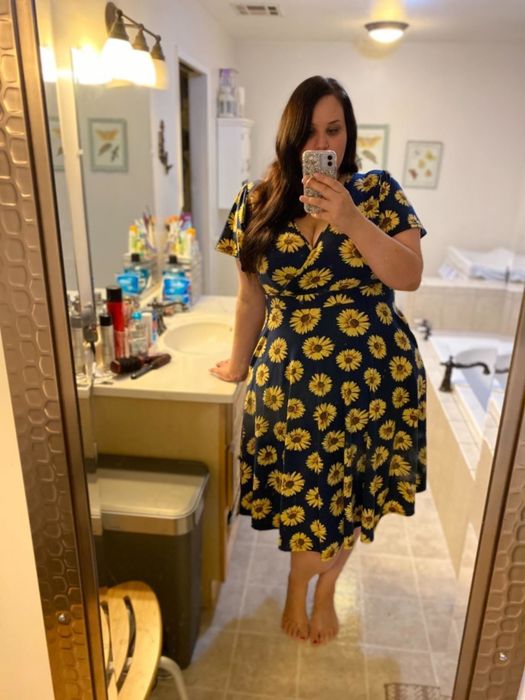 A reviewer wearing a dress adorned with a blue and sunflower print.