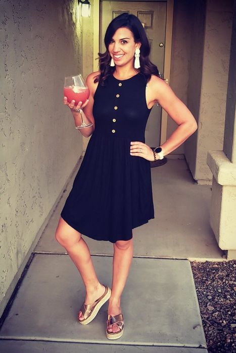 A reviewer wearing the sleeveless, above-the-knee black dress with wooden buttons
