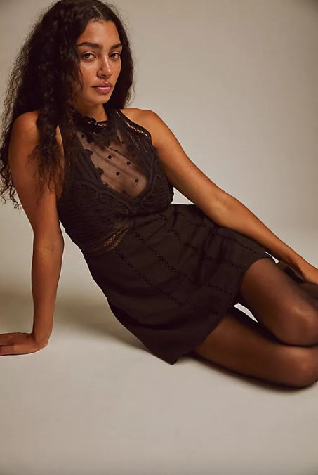 A model wears a black textured mini dress with a sheer dotted panel at the neckline.