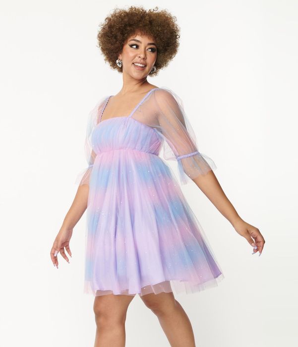 Model wearing a short ombre dress in shades of blue, pink, and purple with sparkles and sheer elbow-length sleeves