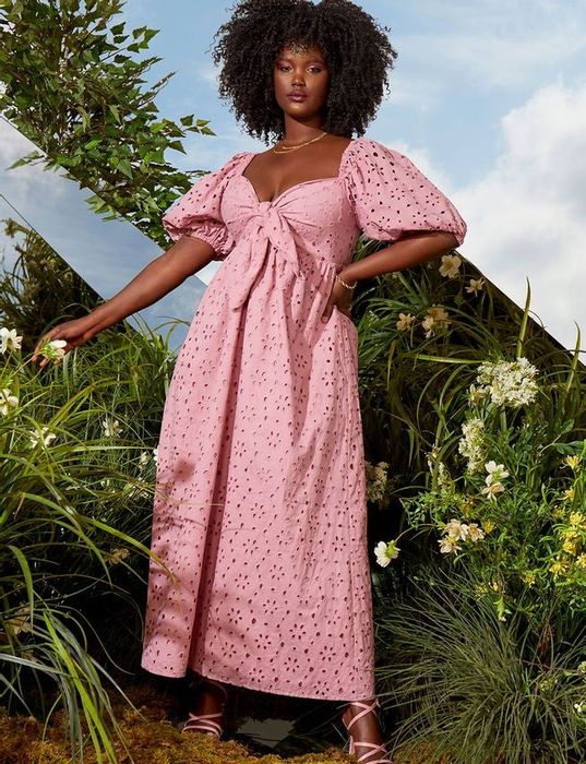 Model wearing a pink eyelet maxi dress with puffed elbow sleeves and a tie at the bust
