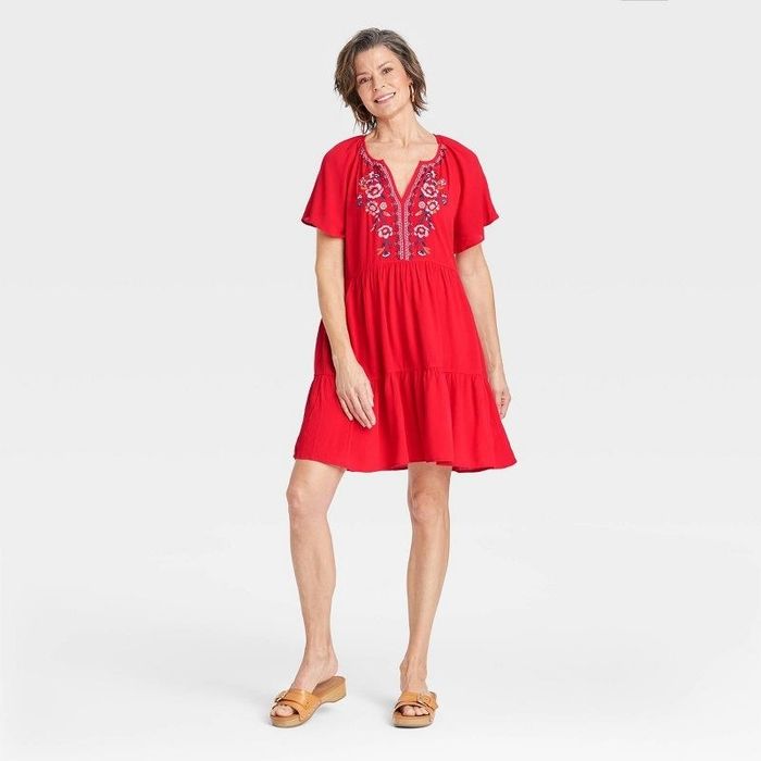 model wearing a bright red dress adorned with intricate designs on the front
