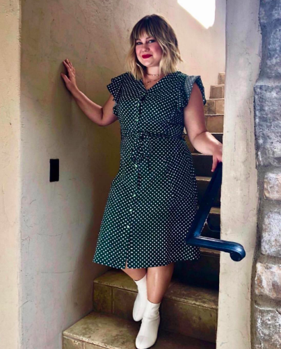 A reviewer modeling the green and white polka dot dress with ruffled short sleeves, a tie waist, and a hemline just below the knee