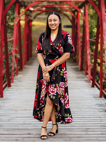 The reviewer is wearing a black maxi wrap dress adorned with red and pink floral patterns throughout.