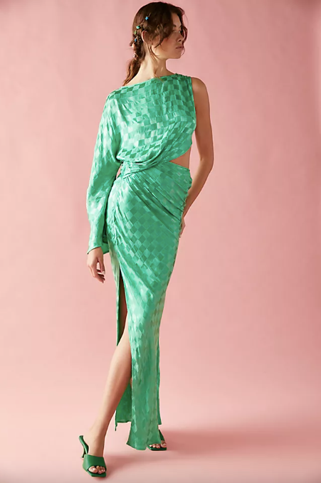 Model wears a stunning green draped gown with a one-shoulder design, a slit, and a side cutout.