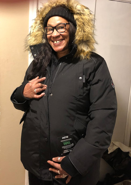 Reviewer smiling while wearing a winter coat with a fur-lined hood, posing indoors