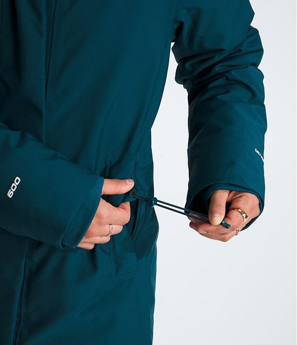 Person adjusting the fit of a teal winter coat with side drawstrings. The coat has a snug, padded design, perfect for cold temperatures