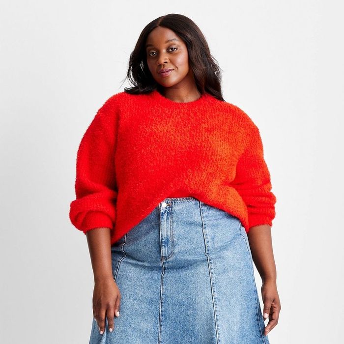 A person wearing a textured sweater and denim skirt, confidently striking a pose.