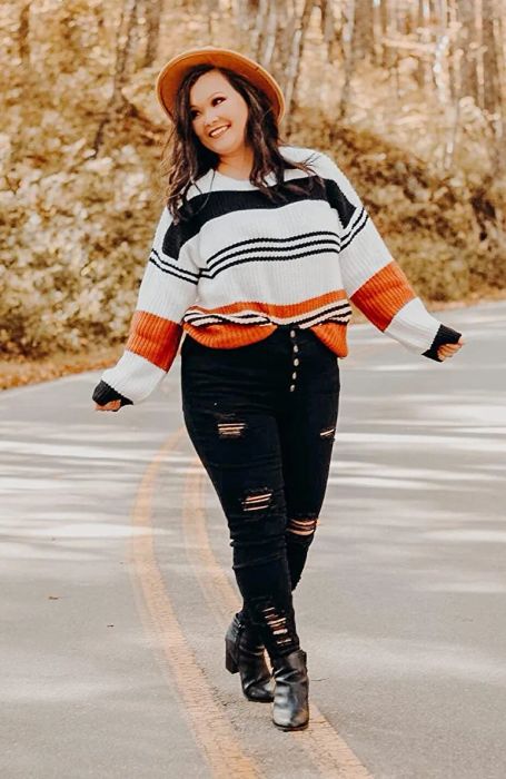 A reviewer wearing the sweater with white, black, and orange stripes