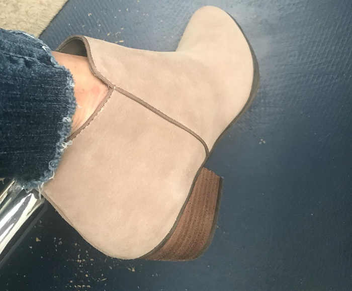 A reviewer showcasing beige suede ankle boots with a chic wooden heel
