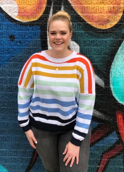 A reviewer wearing the same sweater featuring a white base with rainbow stripes