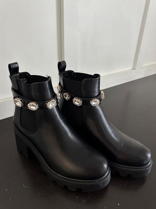 Black ankle boots with chunky heels, highlighted by a decorative strap embellished with oval details around the ankle