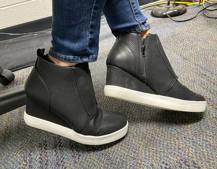 A person wearing sleek black wedge sneakers
