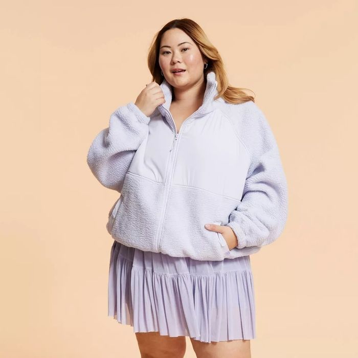 A person wearing a plush oversized fleece jacket paired with a pleated skirt.