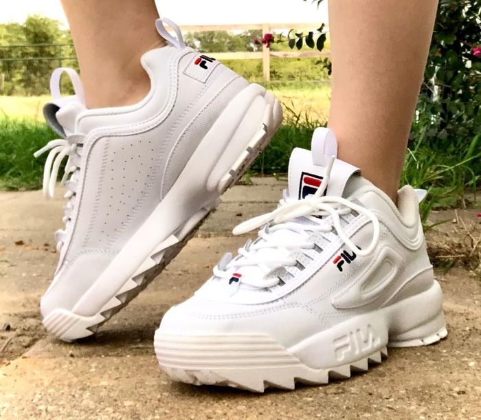 A reviewer pointing their toe to highlight the platform detail of their white sneakers