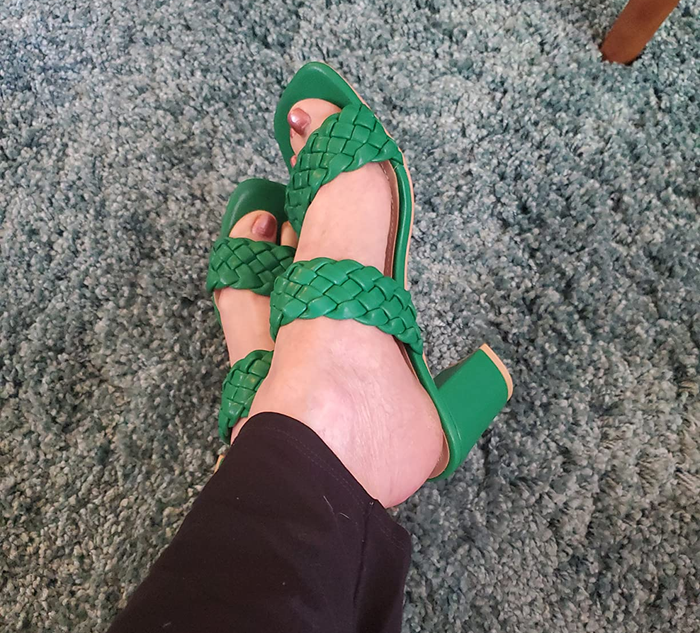 A reviewer modeling green high-heeled sandals with woven straps