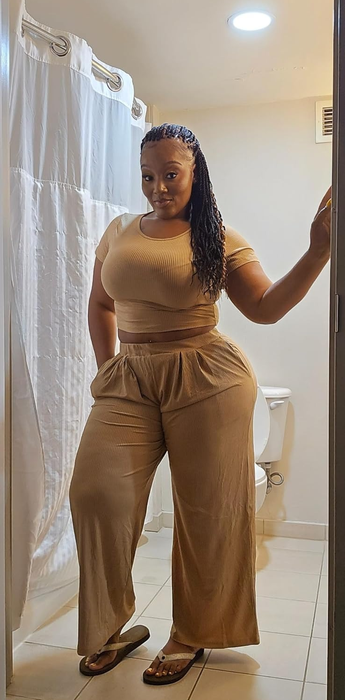 A reviewer wearing a chic fitted top and wide-legged pants, confidently posing in a bathroom