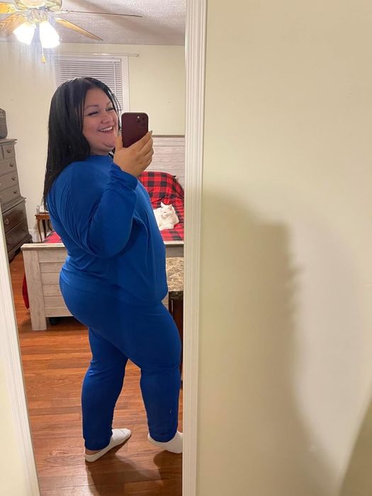 A reviewer in blue loungewear taking a mirror selfie in a bedroom with wooden floors and white walls