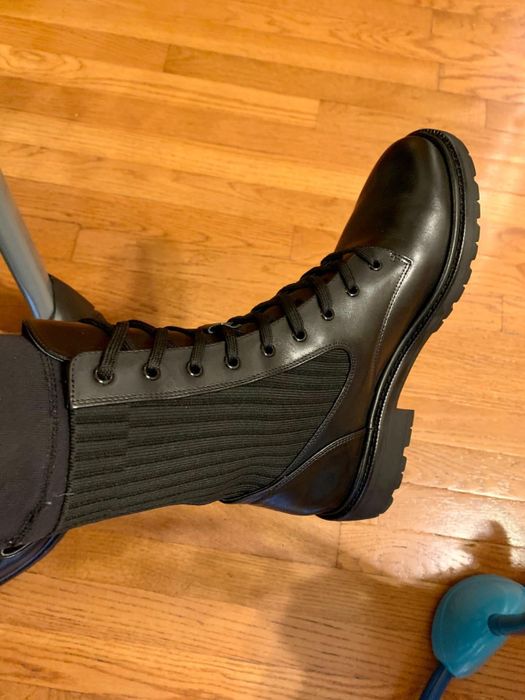 A side view of stylish black leather lace-up boots with ribbed side panels, worn on a wooden floor