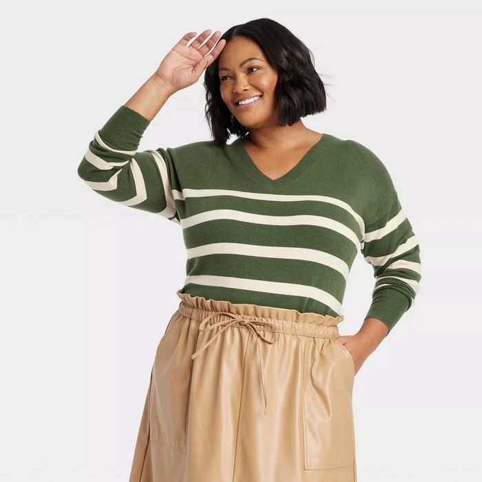 A smiling person wears a V-neck striped sweater and a beige high-waisted skirt.